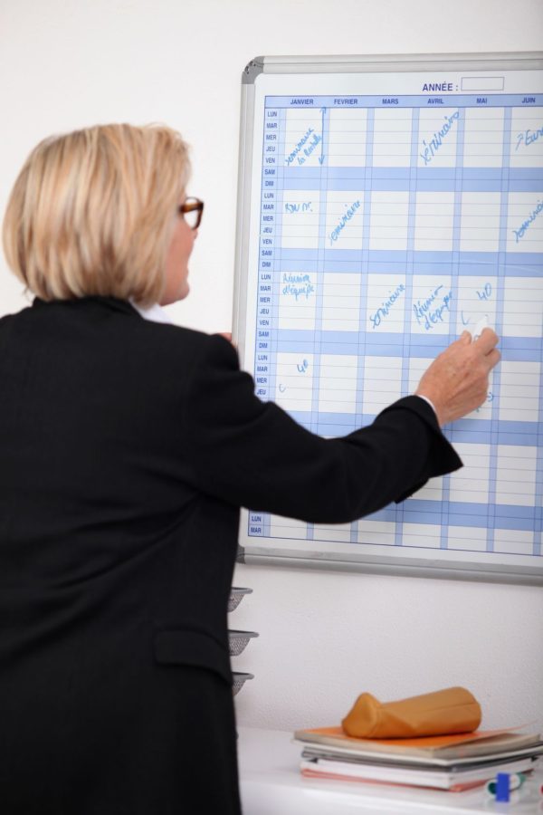 a photo of a businesswoman writing on a wall calendar with a marker, which directs a person's attention to the conveniences of using the Magic Calendar