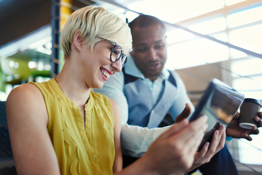 a photo of a white female and a black male looking at the screen of a video tape recorder and discussing about the connection between millennials and corporate social responsibility