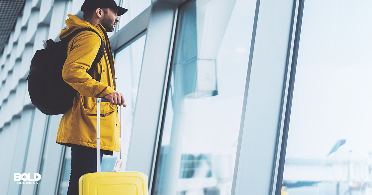 a photo of a traveler staring out a window of an airport, thinking of the future of airline industry