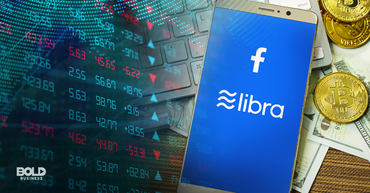 a photo of a phone with its screen open to a digital page showing Facebook's Libra coin logo; the background of the phone is a chart of the stock market figures and a tabletop full of dollar bills and pennies