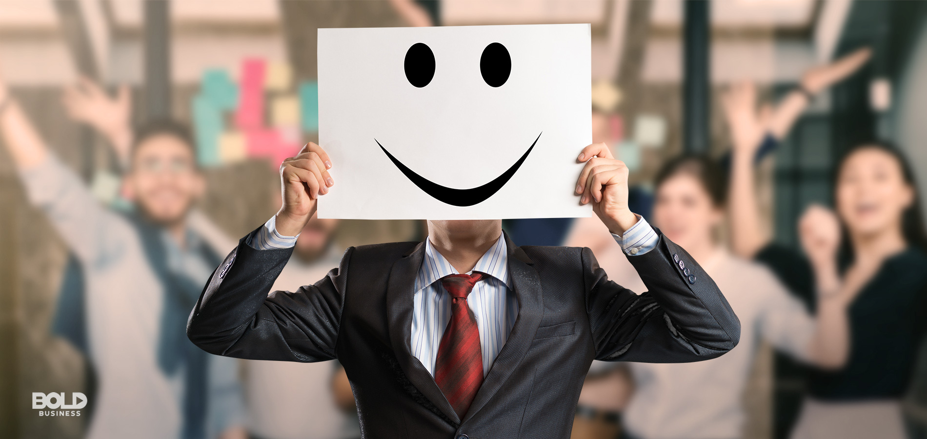 a photo of a man wearing a suit and holding up a white board with a smiley face etched on it, while in front of a blurred photo of a cheering crowd applauding the great employee benefits offered to them