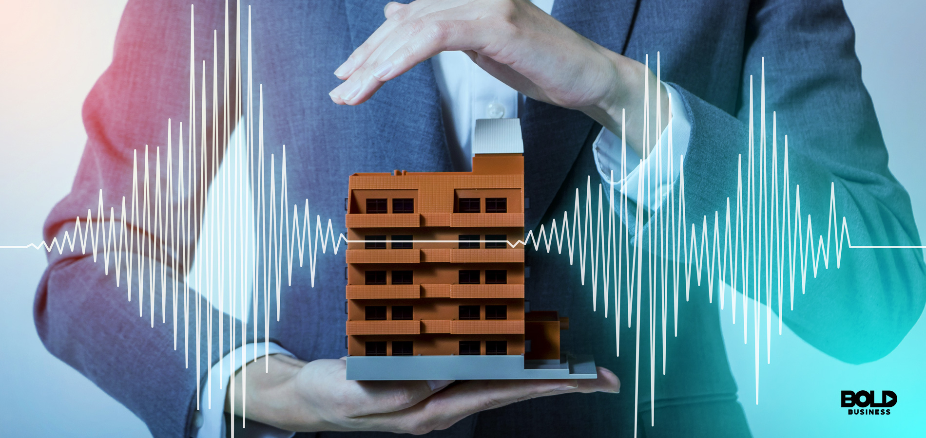 a photo of a business-suited man's whose hands are holding up a small building-like structure amid the topic of soil liquefaction