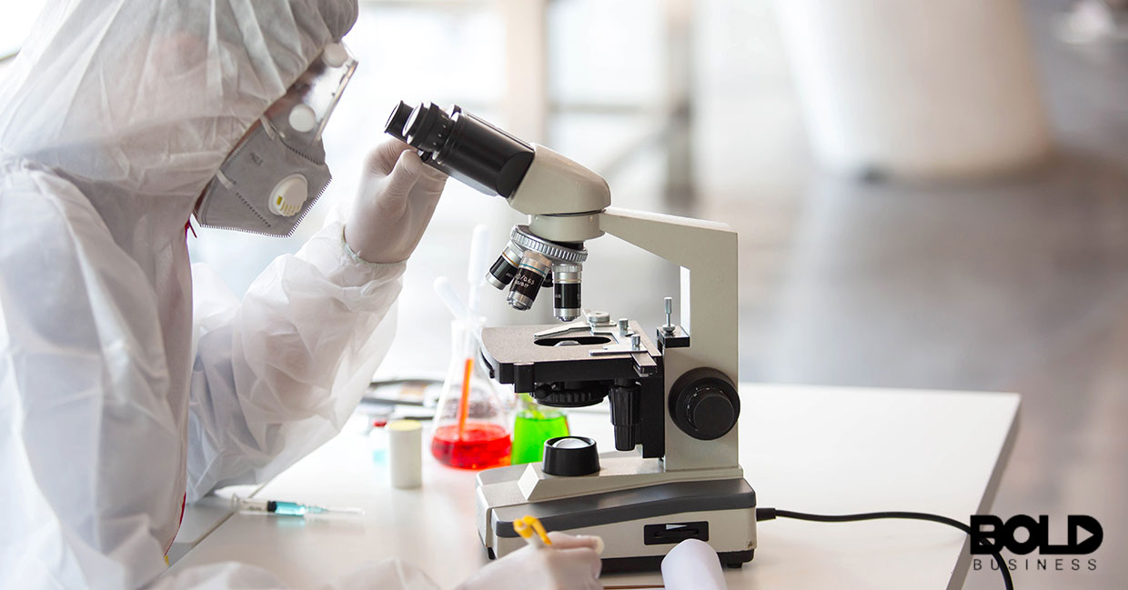 A scientist in full protective gear uses a microscope