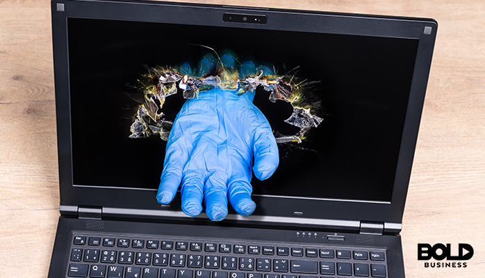 a gloved hand breaking a laptop