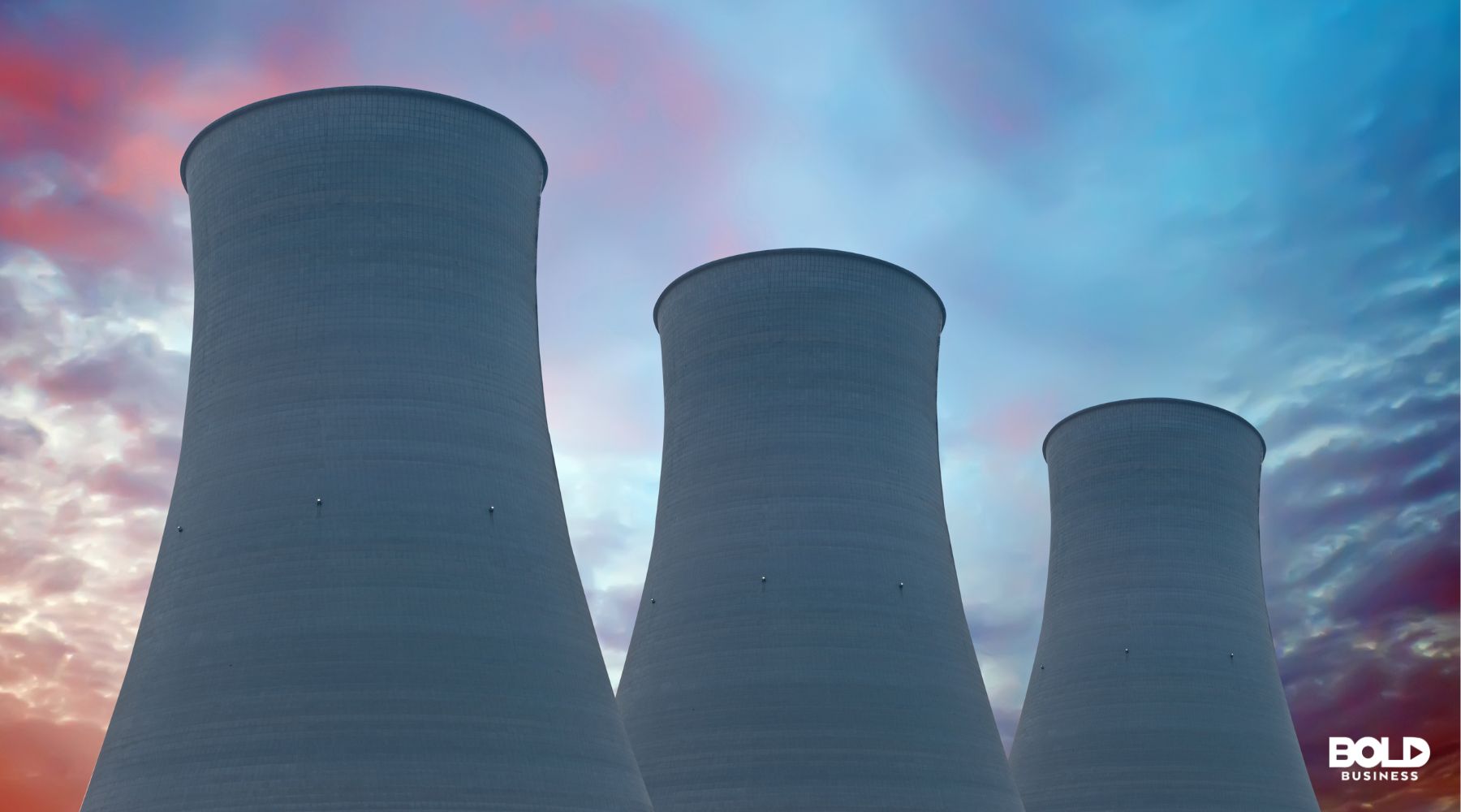 Three large nuclear energy cooling towers rise against a vibrant, colorful sky with hues of blue, pink, and orange, symbolizing industrial energy production.